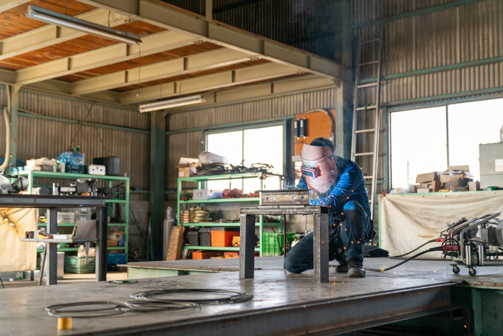 Metal fabrication worker welding in his warehouse.