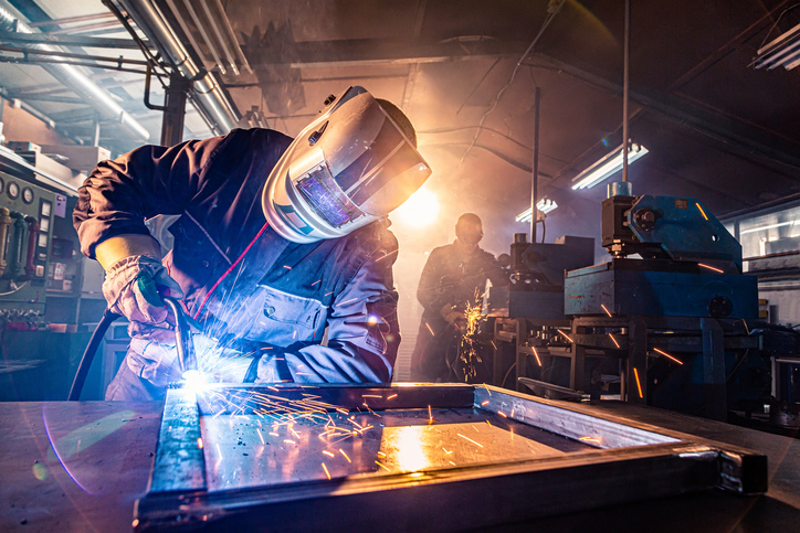 The two handymen performing welding and grinding at their workplace in the workshop, while the sparks "fly" all around them, they wear a protective helmet and equipment. | The Role of Metal Fabrication in CNC Machining