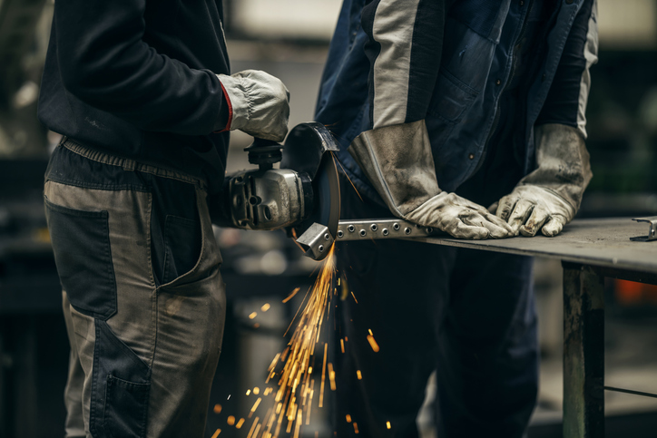 Cropped picture of two metallurgy workers grinding at heavy industry factory.