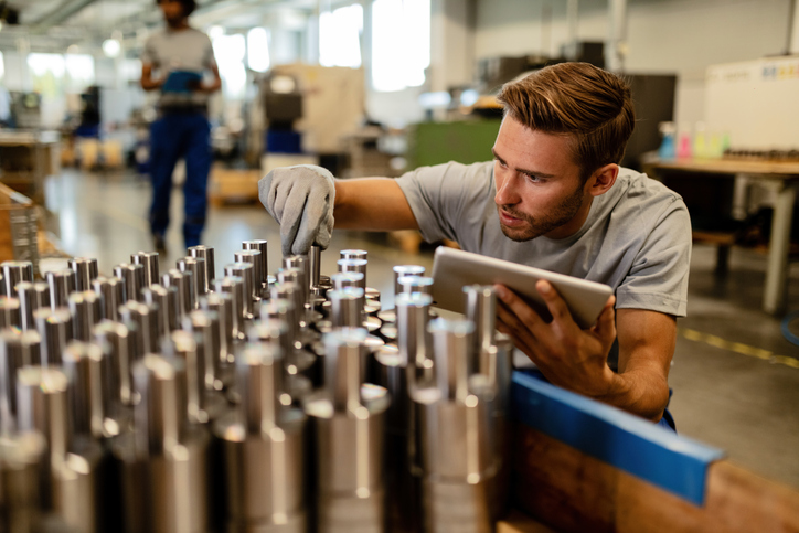 Young metal worker using touchpad while examining steel rods in a factory before the distribution.