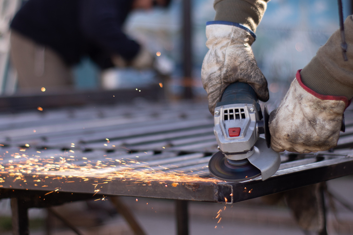 Hands using a cordless angle grinder to fix a metal fence