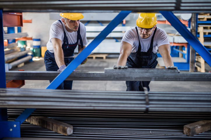 Mid adult steel workers cooperating while working with metal in a factory.