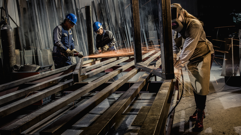 Two senior men and woman using welding torch and welder's visor while welding in workshop.