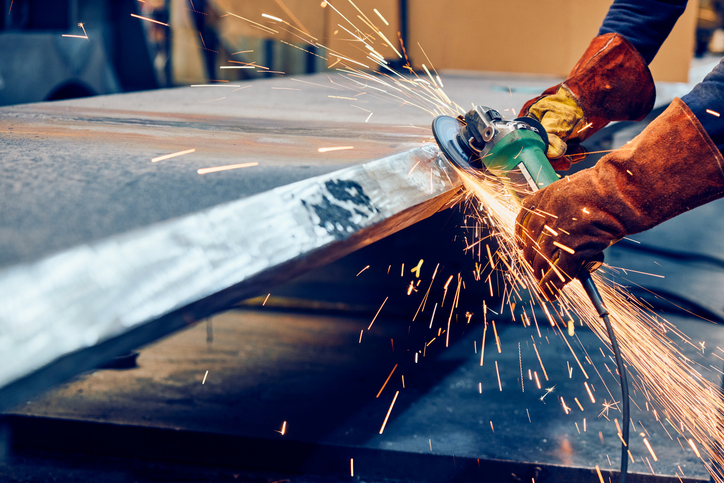 Industrial worker grinding metal surface with angle grinder