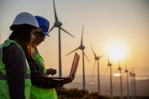 Young maintenance engineer team working in wind turbine farm at sunset